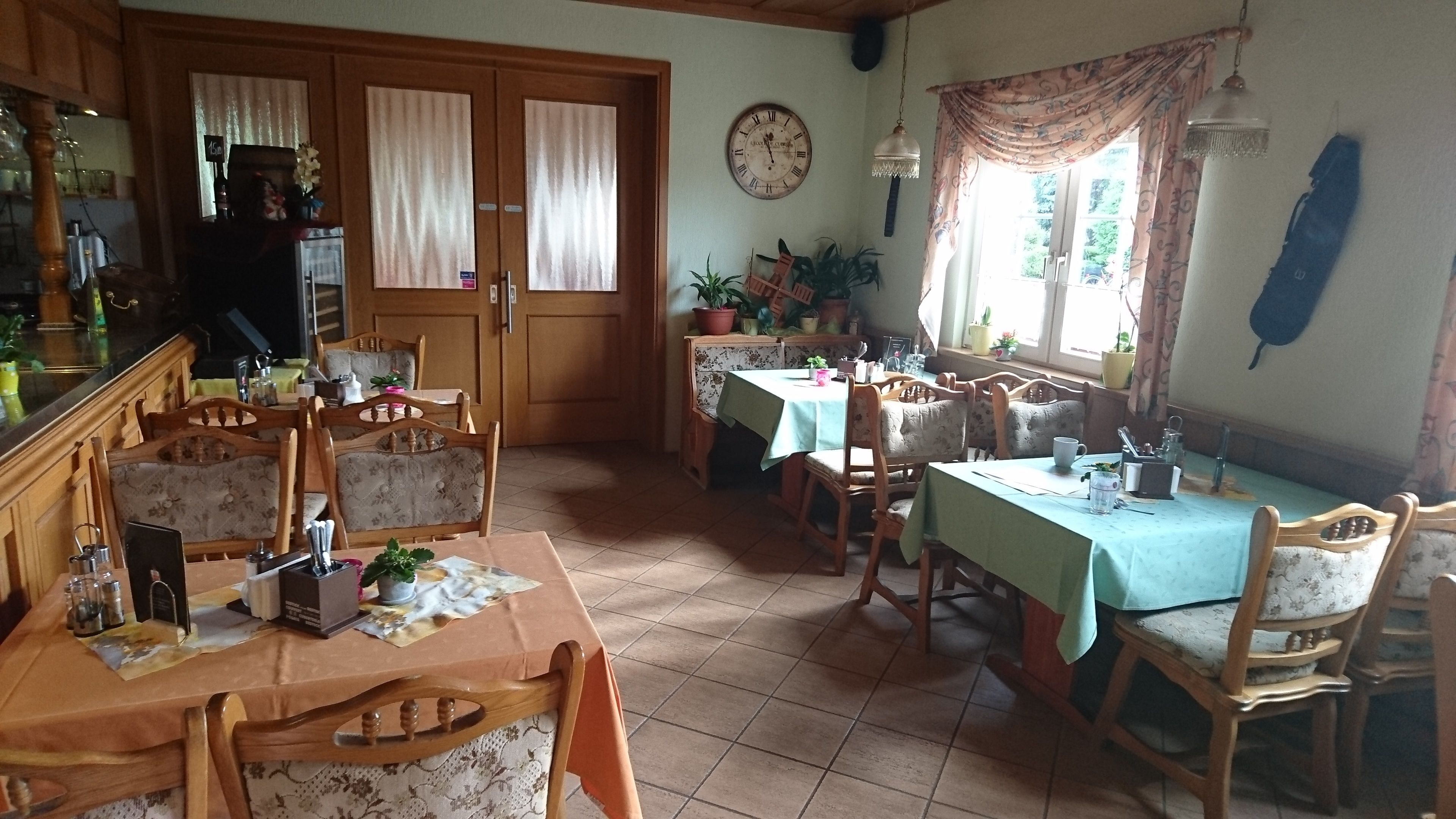 A dining area with wooden tables and chairs, a clock on the wall, and potted plants.