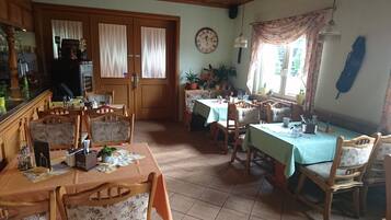 A dining area with wooden tables and chairs, a clock on the wall, and potted plants.