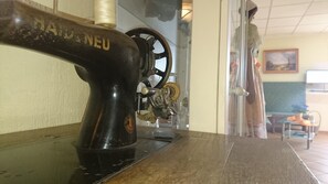 Eine alte Nähmaschine mit schwarzem Korpus und goldener Beschriftung steht auf einem Holztisch in einem Raum mit einem grünen Sofa und einem Bild an der Wand.