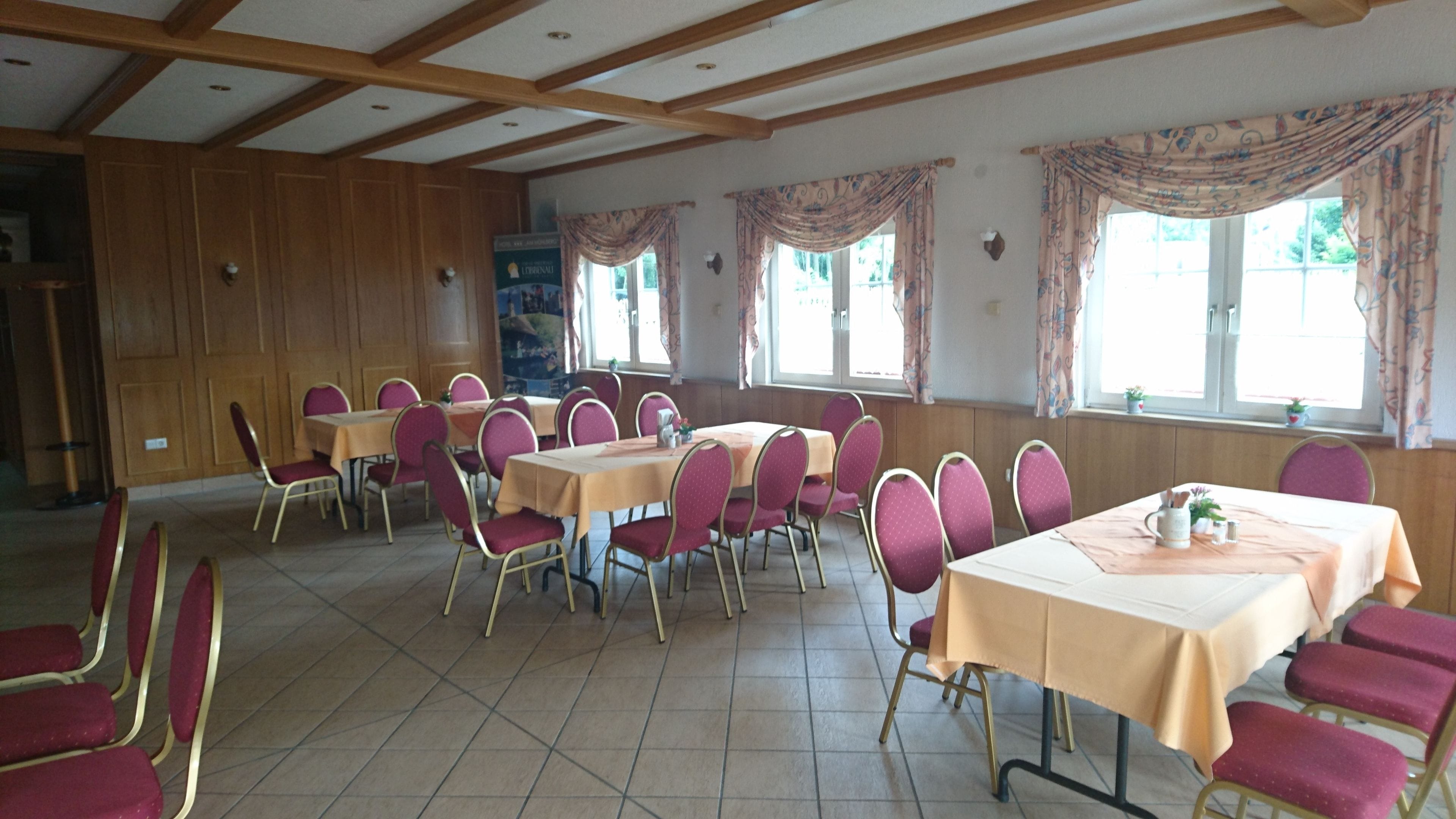 Un espace repas comprenant plusieurs tables et chaises, des lambris en bois sur les murs et de grandes fenêtres avec des rideaux.