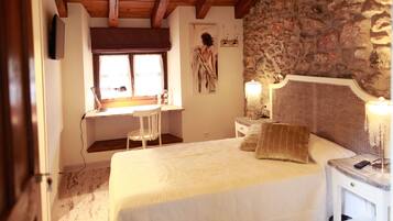Un dormitorio con cama, escritorio, silla, lámpara y pared de piedra.