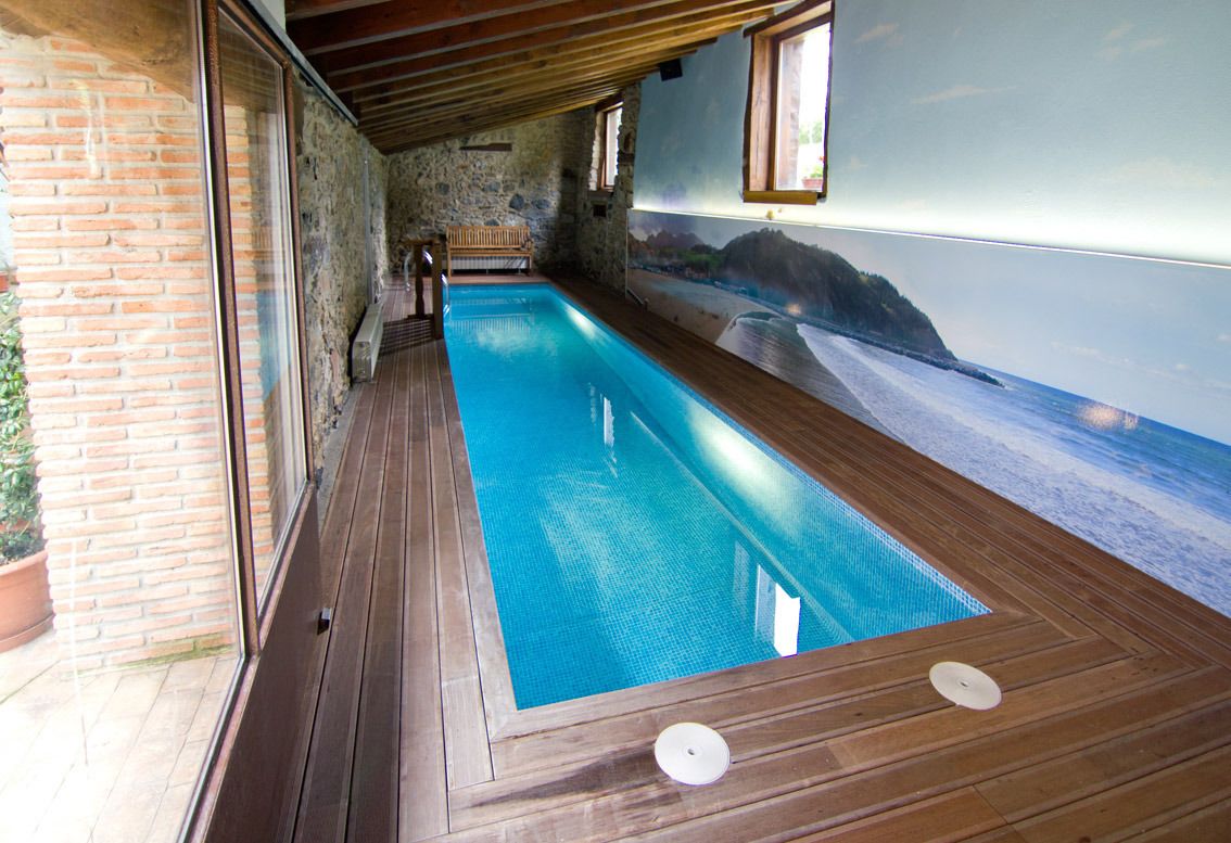 Una piscina con cubierta de madera, paredes de piedra y un mural con una escena de playa.
