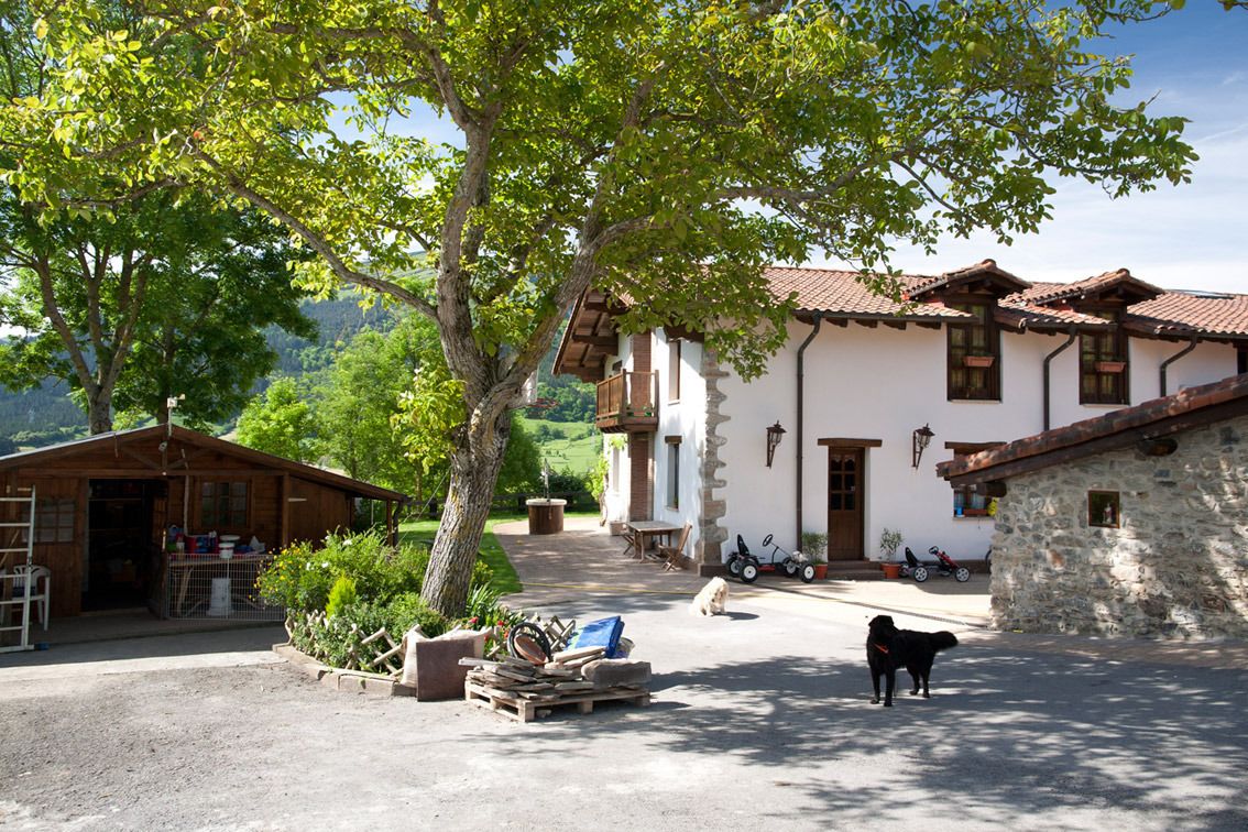 Edifici rústic amb paret de pedra, un porxo de fusta i un arbre al davant.