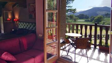 A room with a red sofa, a bed with a tufted headboard, and a balcony with a table and chairs.