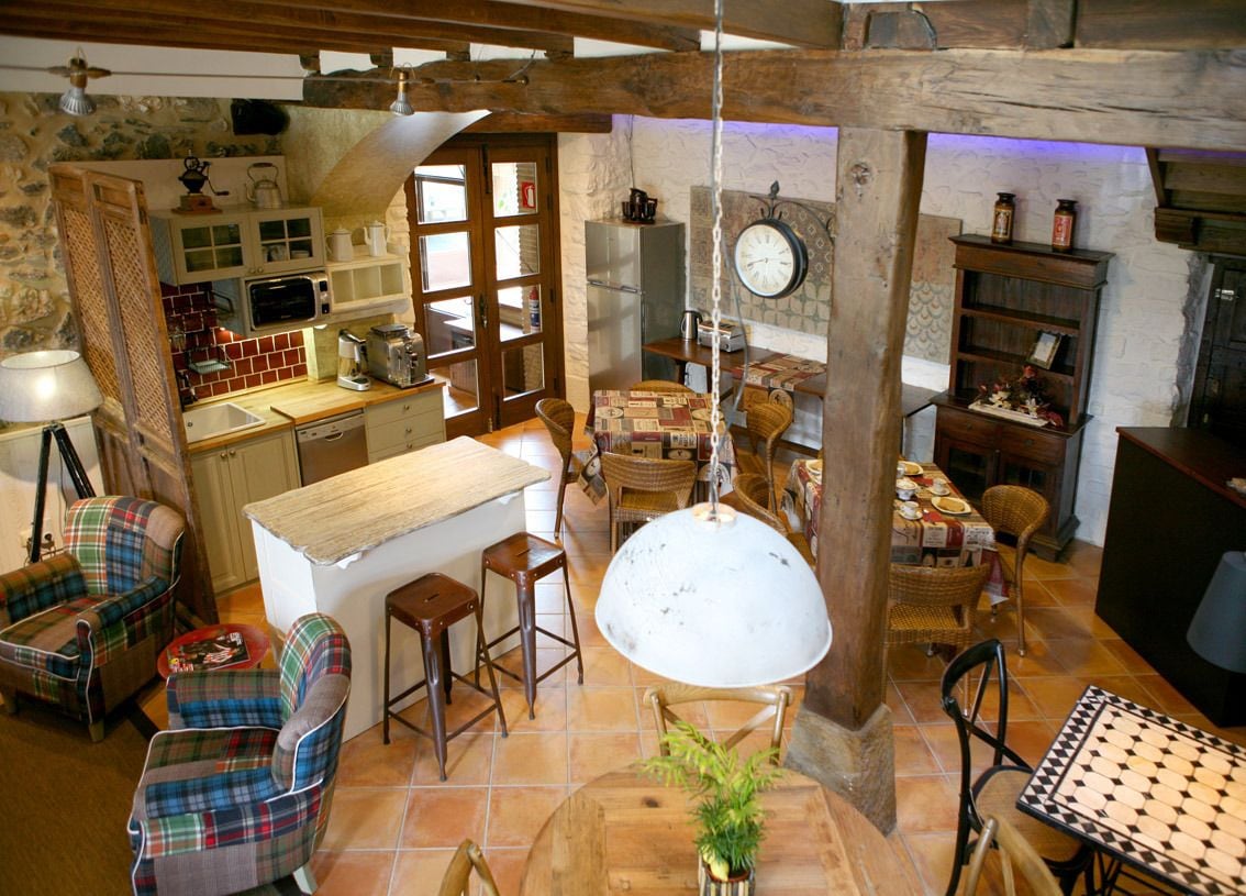 A rustic kitchen with a wooden ceiling, a large hanging light, and a dining area with a round table and chairs.
