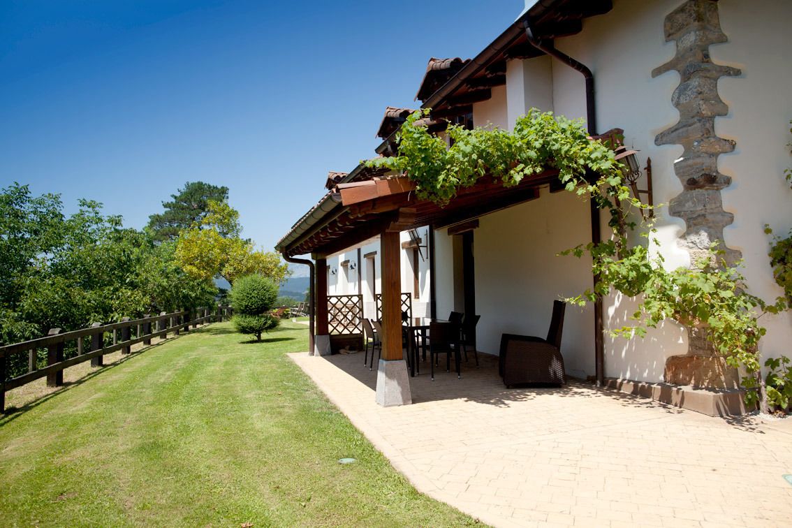 Een gebouw met een overdekt terras, een stenen muur en uitzicht op een pad met bomen.