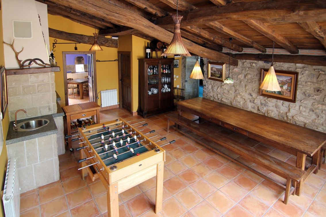 Una habitación rústica con mesa de fútbol de mesa, bancos de madera, paredes de piedra y chimenea de piedra.