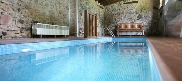 Una piscina interior con paredes de piedra y bancos de madera.