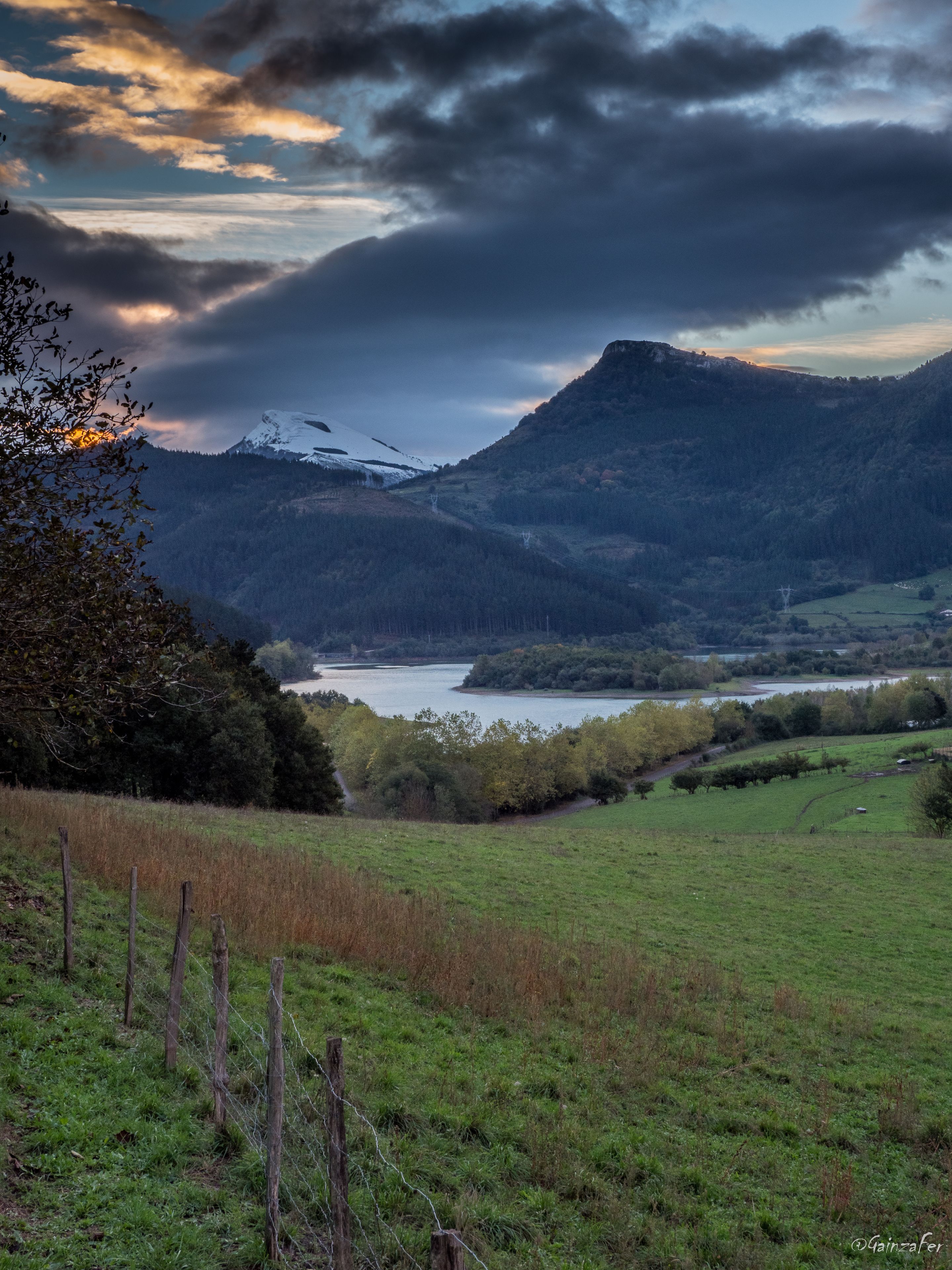 Un paisaje montañoso con un lago, colinas boscosas y un cielo despejado.