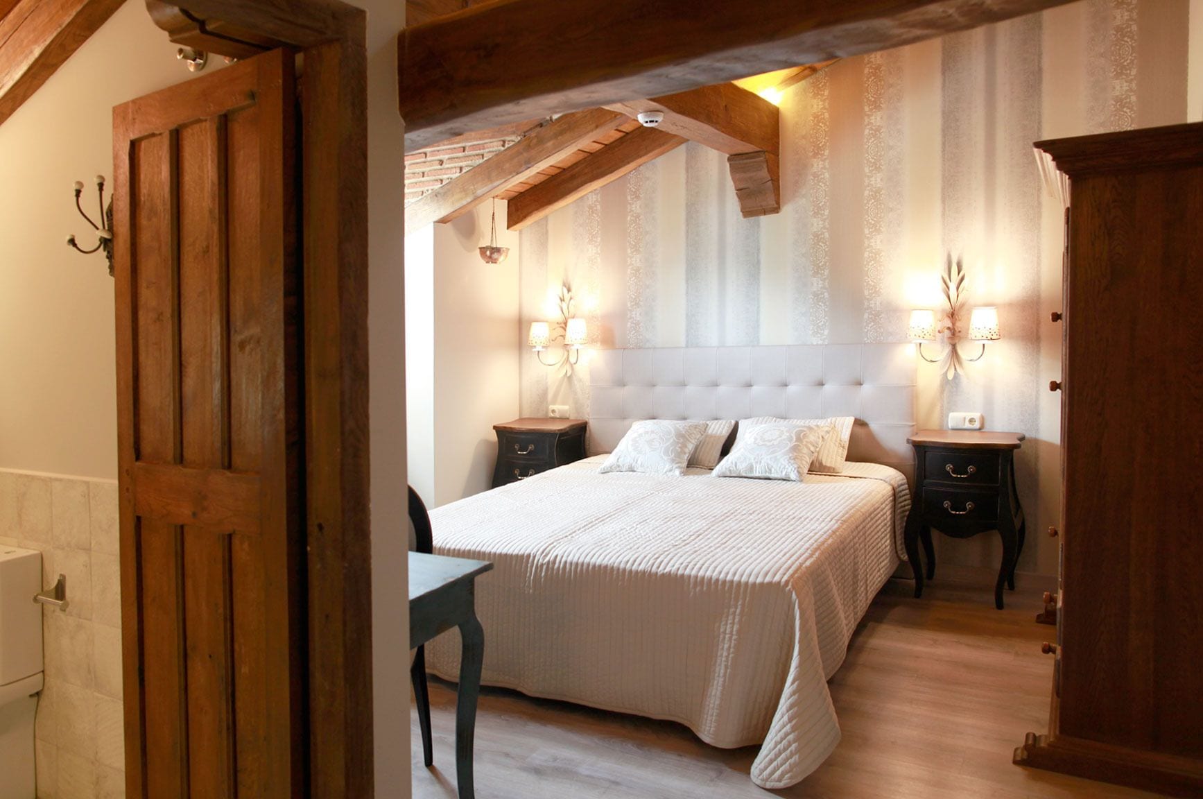 Une chambre à coucher avec un grand lit, deux tables de chevet, une armoire en bois et un lustre.