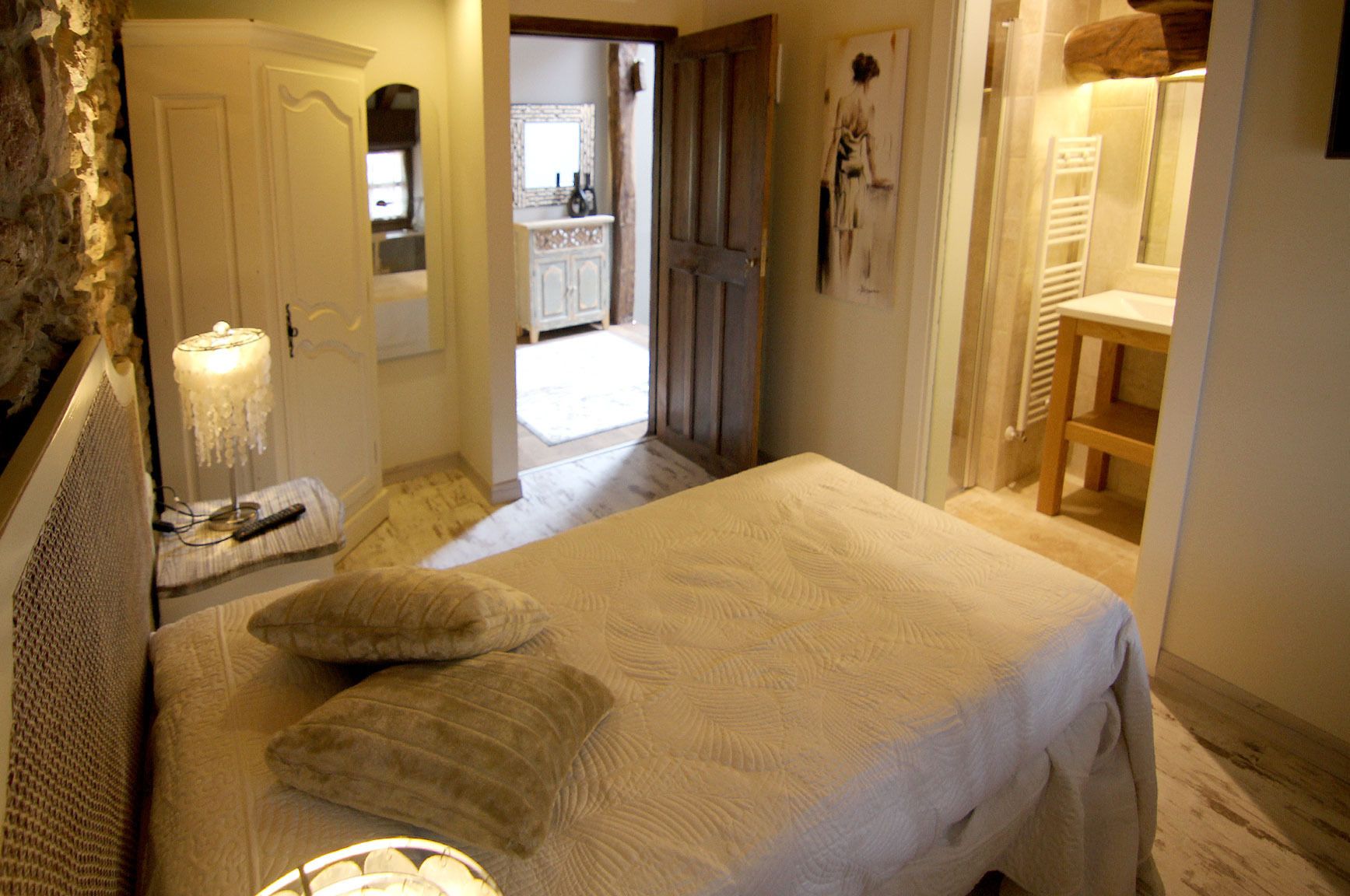 A bedroom with a bed, pillows, a lamp, a dresser, and a door leading to a bathroom.
