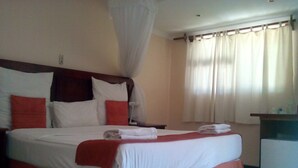 A neatly made bed with a canopy, a bedside table, and a view of a window with curtains. - Northgate Lodge (Nata)