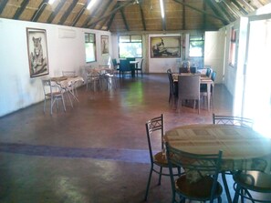 A spacious room with a high ceiling and natural light from windows. There are several tables and chairs arranged for dining or meetings. - Northgate Lodge (Nata)