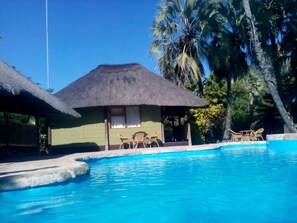 A pool area with a thatched-roof hut and lounge chairs. - Northgate Lodge (Nata)