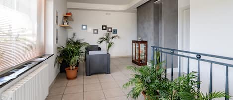 Un balcón amplio con plantas en macetas, una silla de mimbre y un aparador de vidrio.