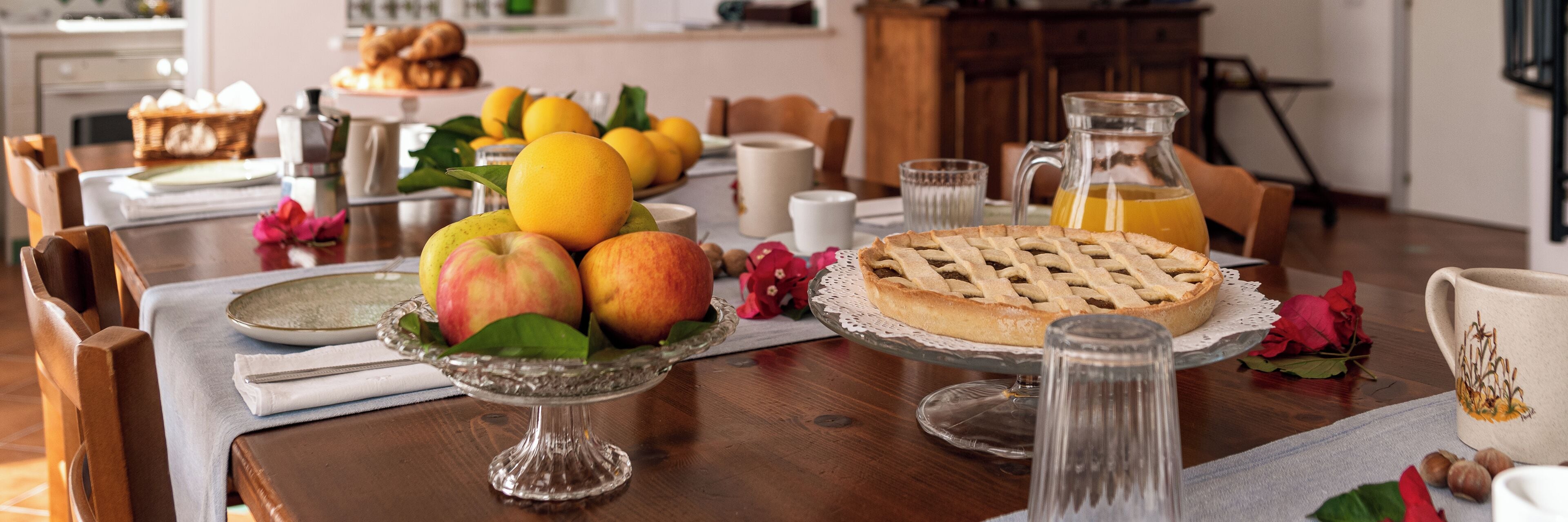 Uma mesa de café da manhã com frutas, uma torta e um jarro de suco de laranja.