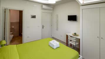 Habitació d'hotel amb un llit verd, un escriptori amb cadira, televisió penjada a la paret i un armari.