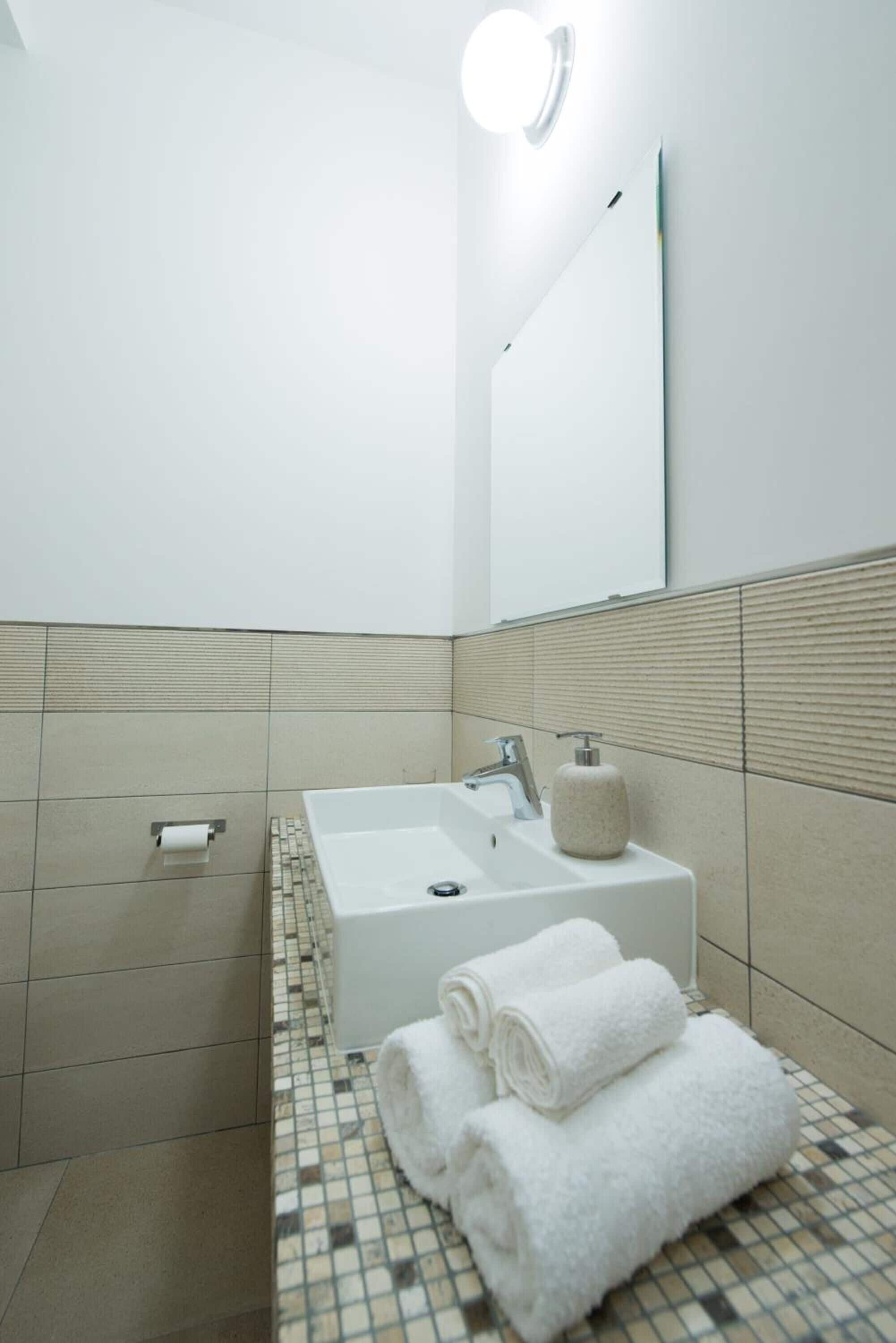 A modern bathroom with a white sink, a mirror, and a tiled floor.