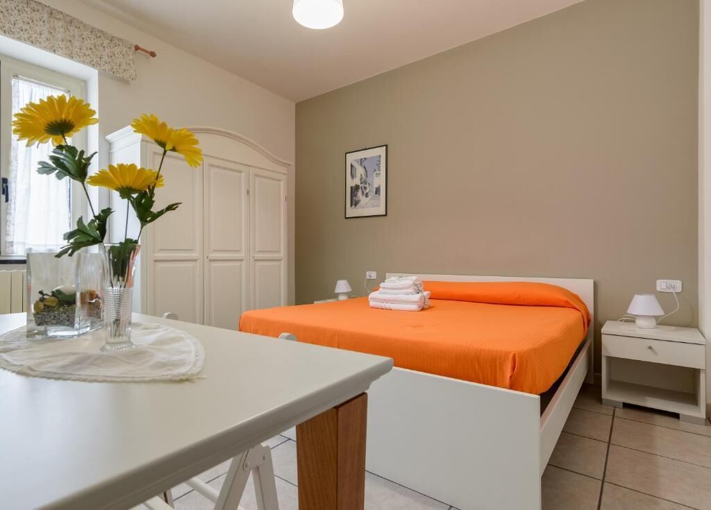 A bedroom with a bed, a nightstand, a table with a vase of flowers, and a window.
