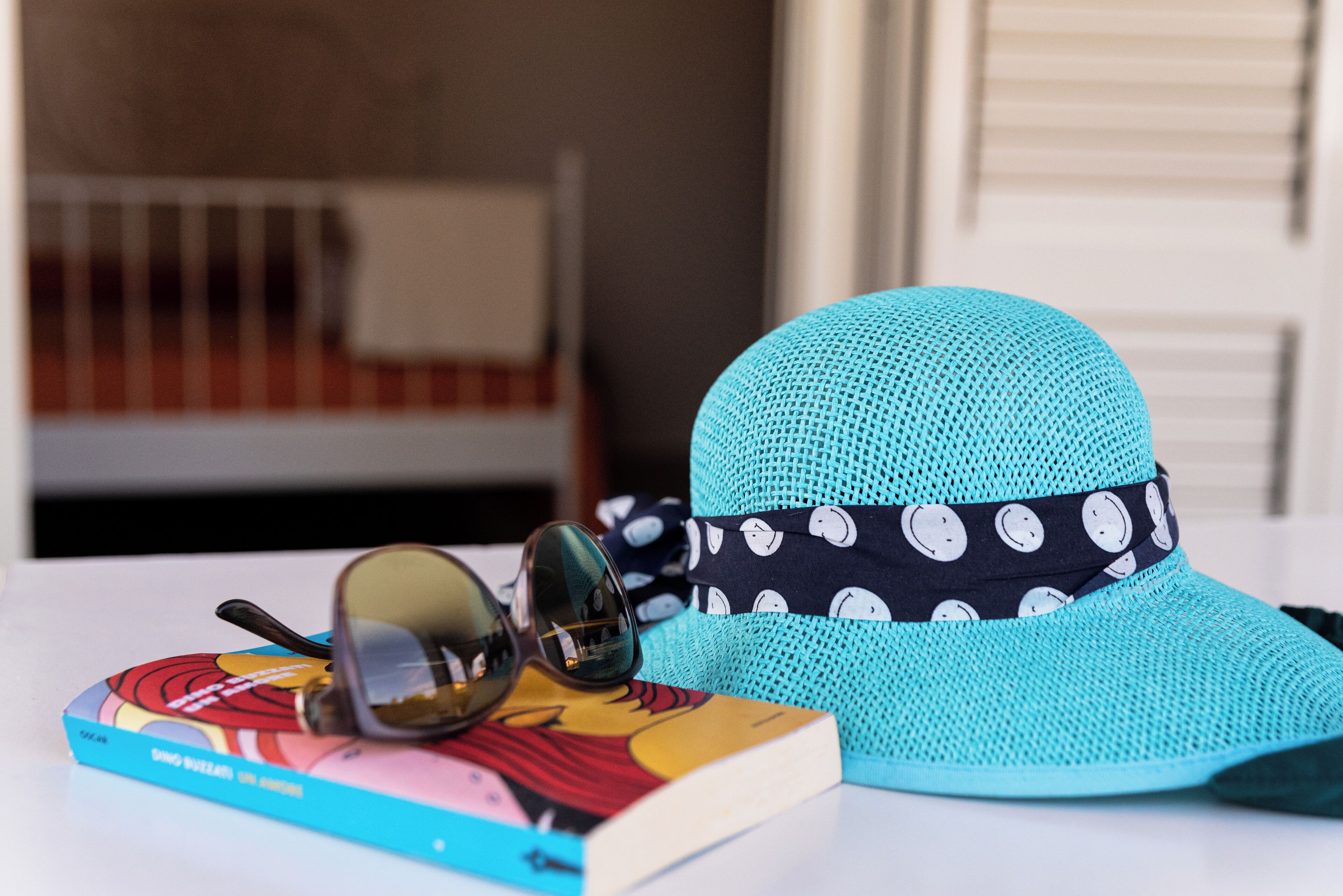 A turquoise hat with a polka dot band, a pair of sunglasses, and a colorful book on a white surface.