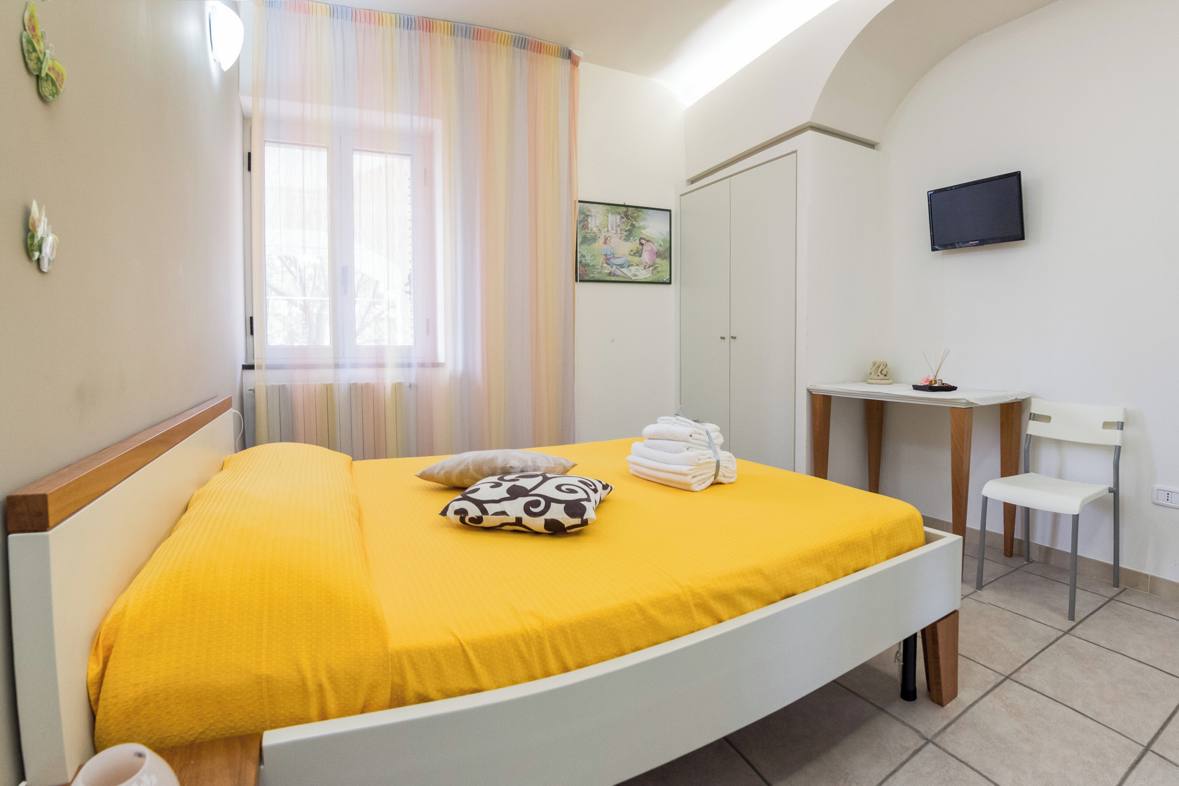 Une chambre avec un lit, un bureau, une chaise, une télévision et une fenêtre avec des rideaux.
