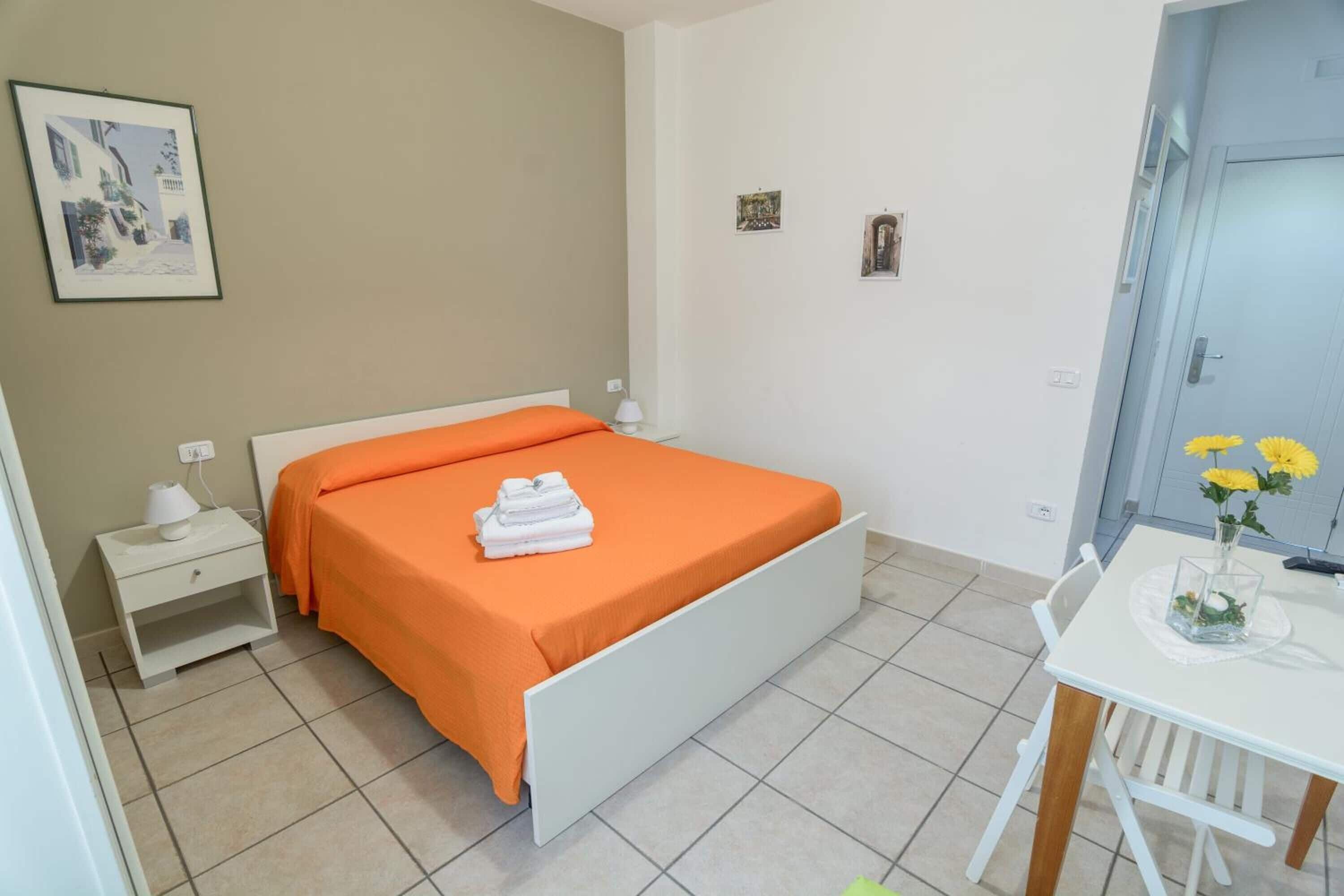 A bedroom with a bed, a nightstand, a table with a vase of flowers, and a door.
