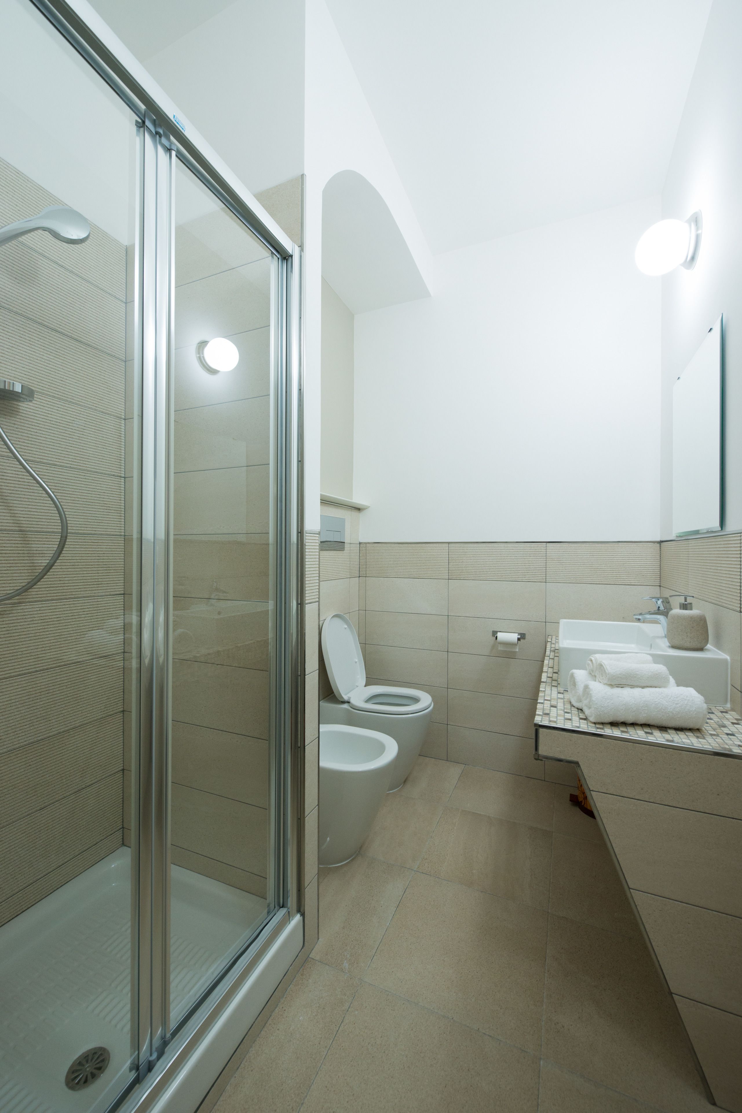 A modern bathroom with a glass-enclosed shower, a toilet, and a sink area with towels.