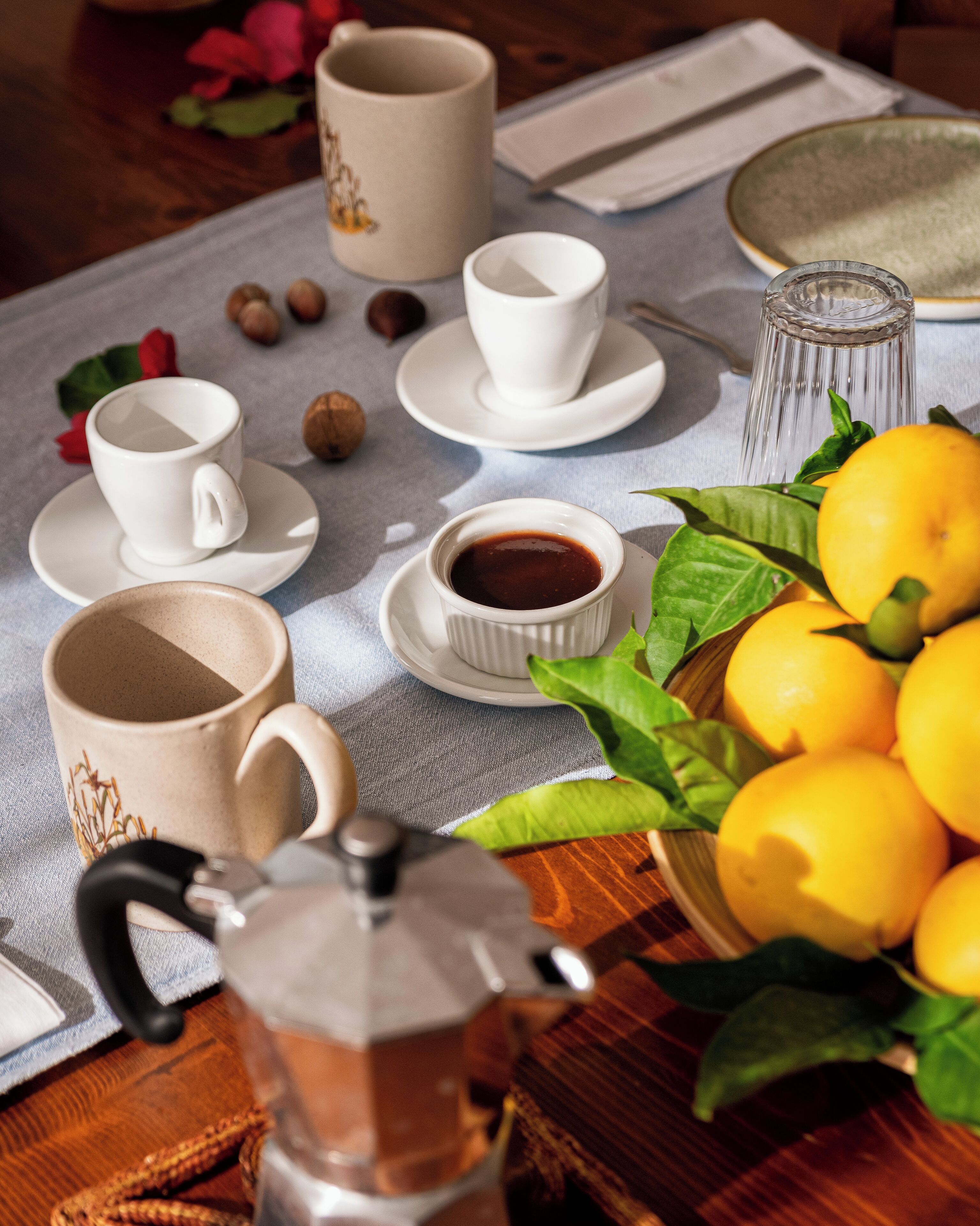 A table with a coffee pot, cups, saucers, a bowl of lemons, and a glass pitcher.