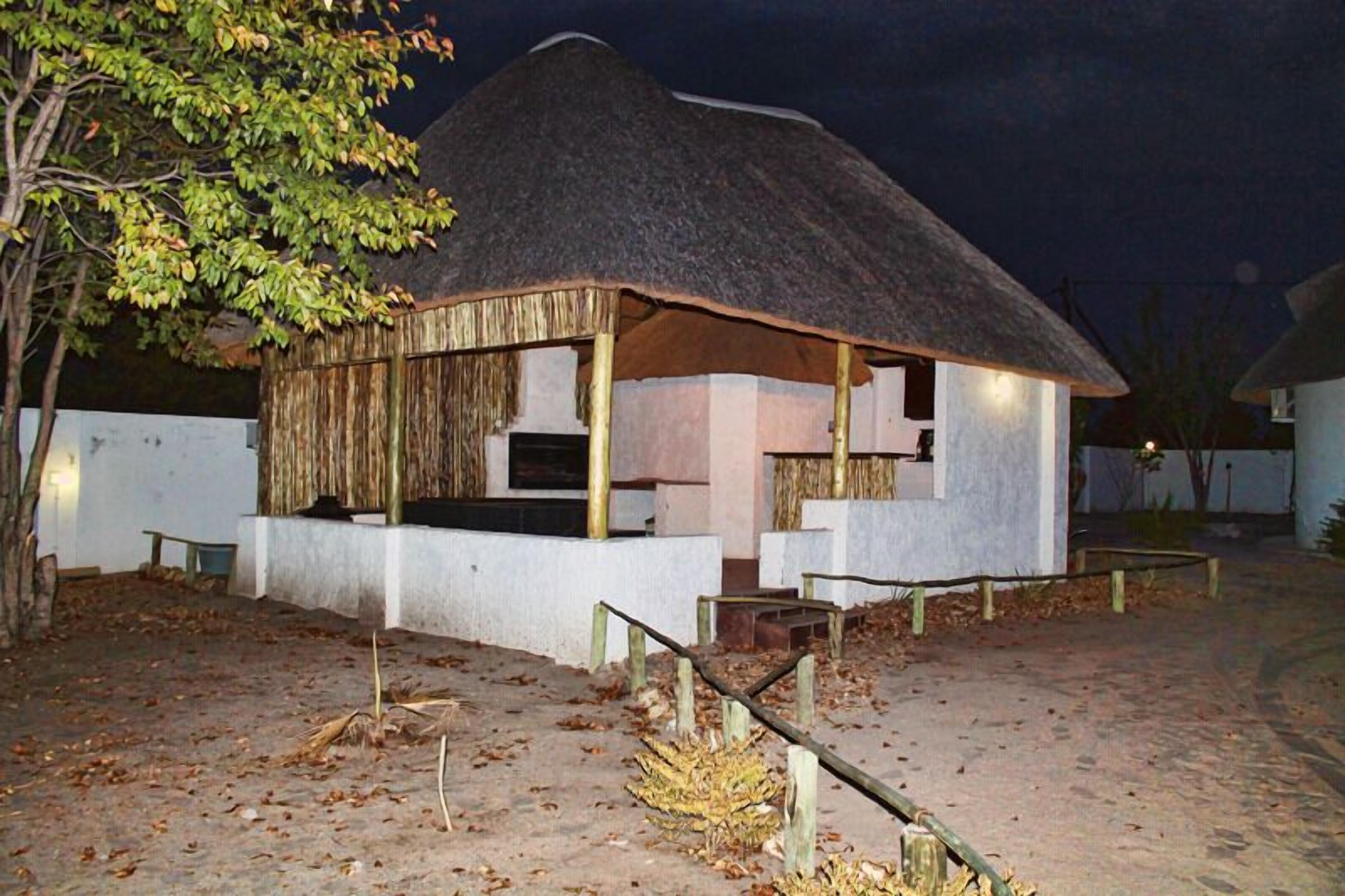 A thatched-roof hut with a white exterior, surrounded by a fence and leaf-covered ground.
