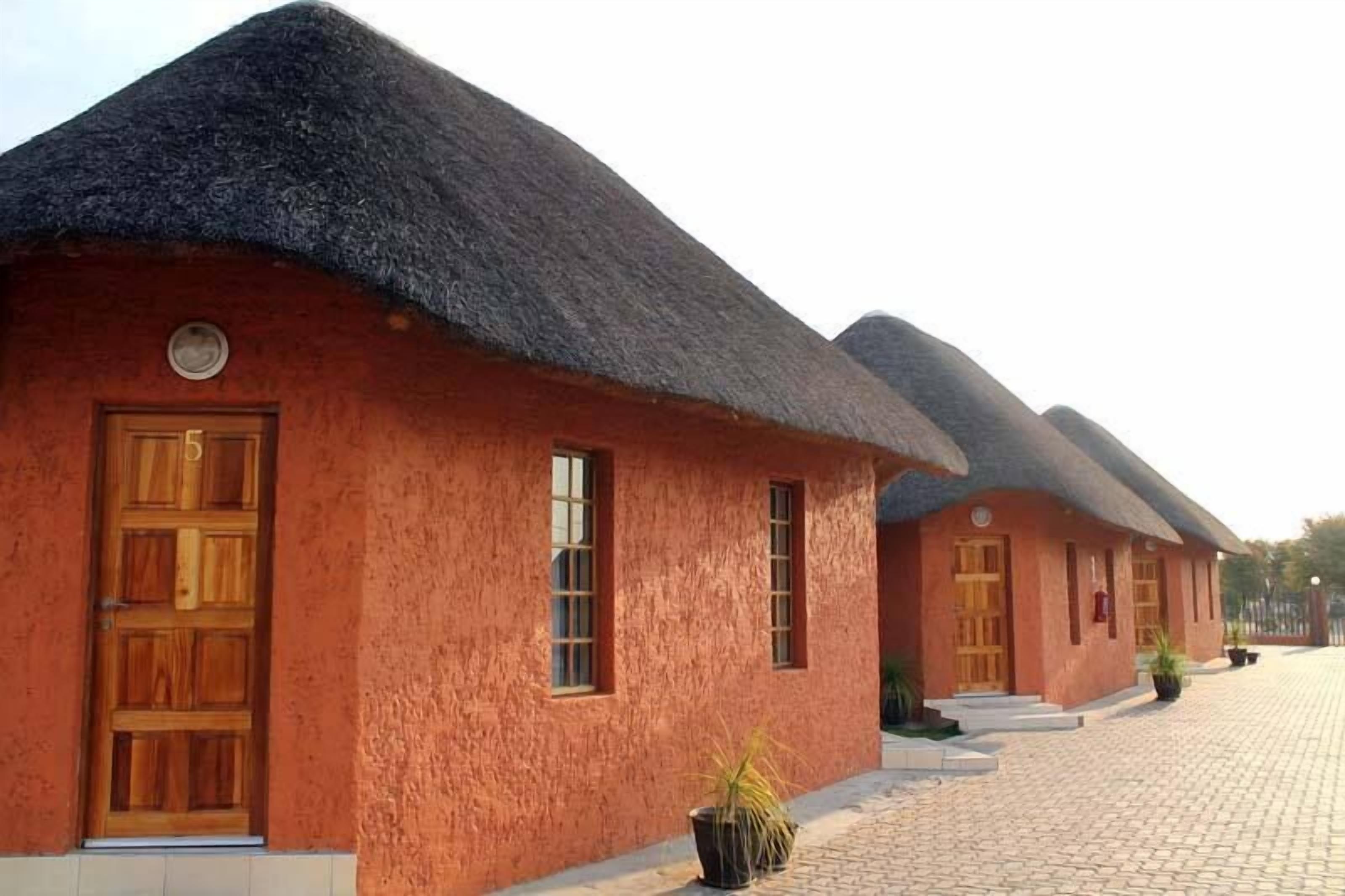 A row of traditional thatched-roof cottages with wooden doors and windows, arranged along a paved pathway.