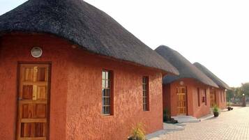 A row of traditional thatched-roof cottages with wooden doors and windows, arranged along a paved pathway.