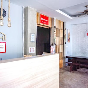 A reception area with a wooden reception desk, a red sign above the door, and a ceiling fan. - RedDoorz near Lippo Mall 2 (Kuta)