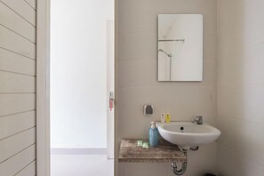 A bathroom with a white sink, a mirror, and a wooden shelf with toiletries. - RedDoorz @ Pecatu Ungasan (Ungasan)