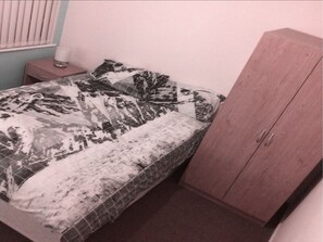 A bedroom with a bed covered in a patterned bedspread, a wooden wardrobe, and a bedside table with a lamp. - The L6 Guest Rooms (Liverpool)