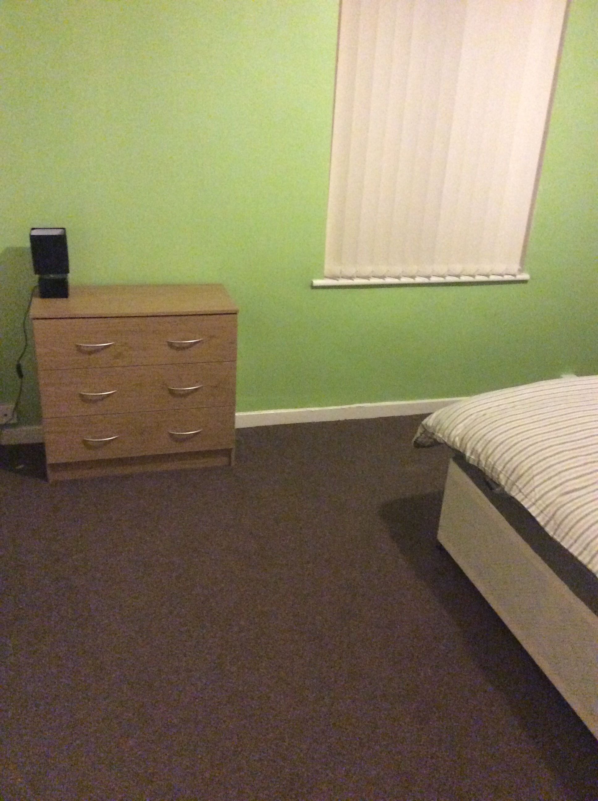 Une chambre à coucher avec un lit, une commode et une fenêtre équipée de stores.