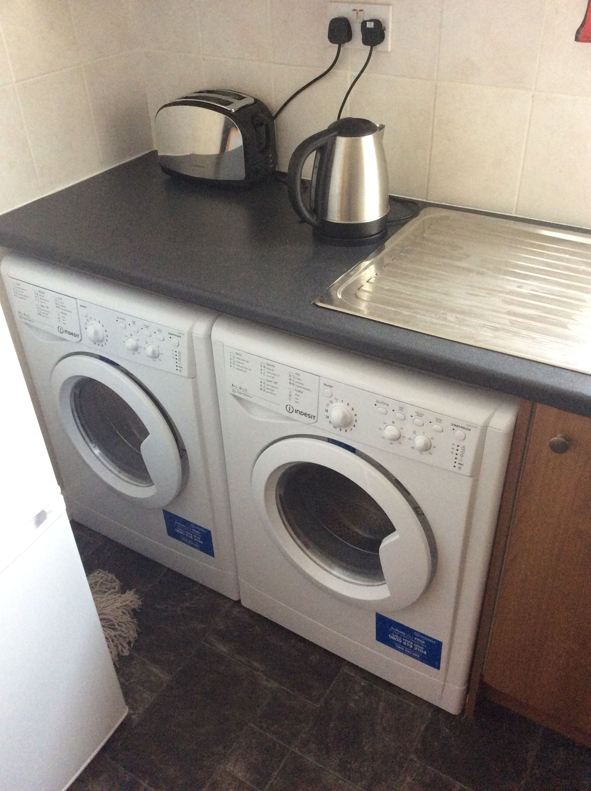 A compact laundry area with two front-loading washing machines and a toaster on a countertop.
