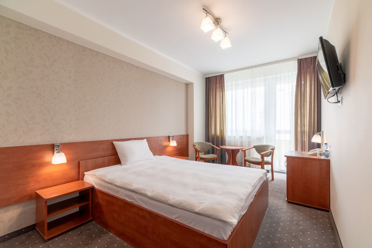 A hotel room with a wooden bed, bedside tables, a desk, a chair, and a television.