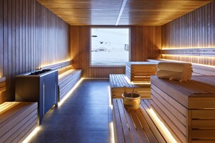 A sauna with wooden walls and benches, a bench with a towel, and a wooden bucket.
