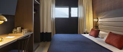 A hotel room with a bed, a desk with a chair, a television, and a window with curtains.