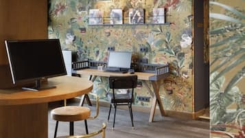 A workspace with a computer, a monitor, and a chair. There is a wall with a floral pattern and shelves with items on them.