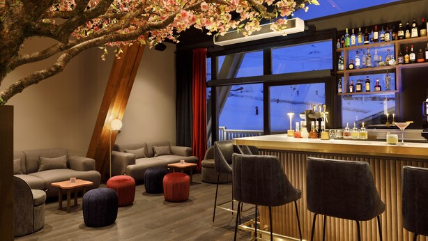 A bar area with a wooden counter, bar stools, and a large window with a view.