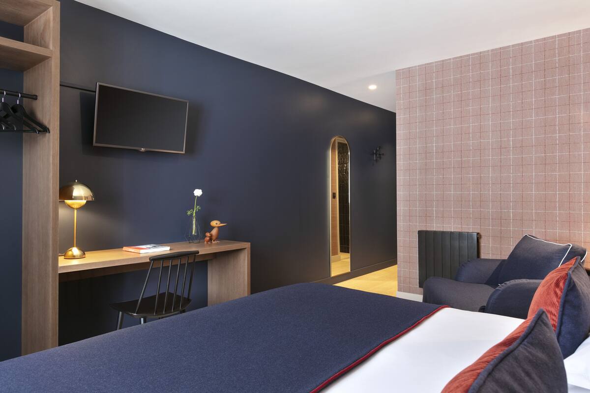 Una habitación de hotel moderna con una cama, un escritorio, una silla y un televisor fijado a la pared.