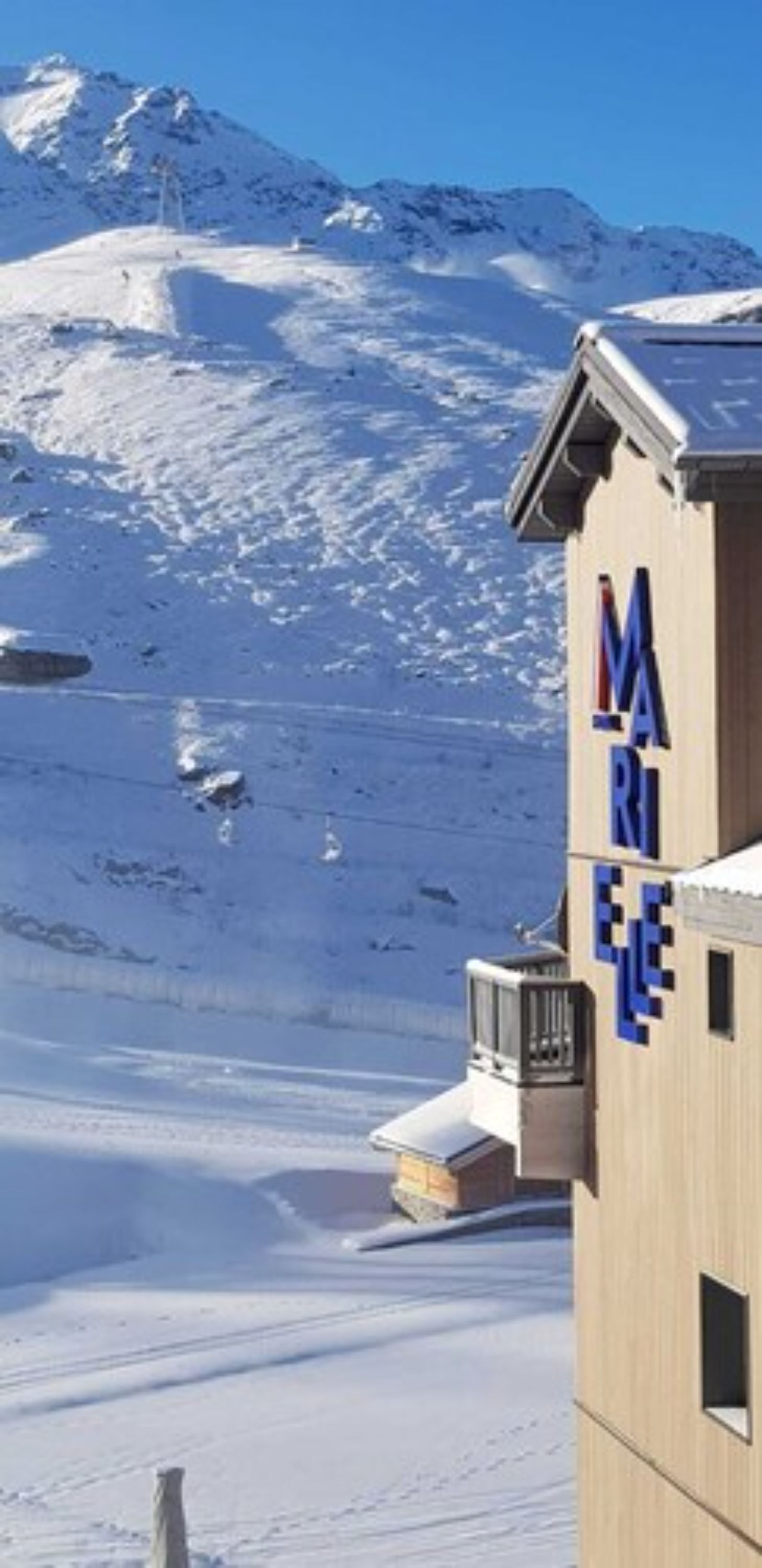 A building with the sign 'MARIE' in large letters, set against a snowy mountain backdrop.