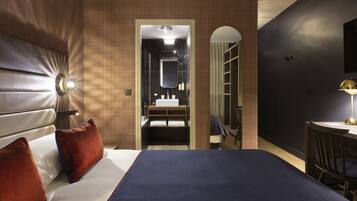 Camera d'albergo con un letto, una scrivania, una sedia, uno specchio e un bagno visibile attraverso un arco.