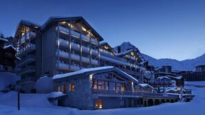 A multi-story hotel with balconies, a snow-covered roof, and a mountainous backdrop.