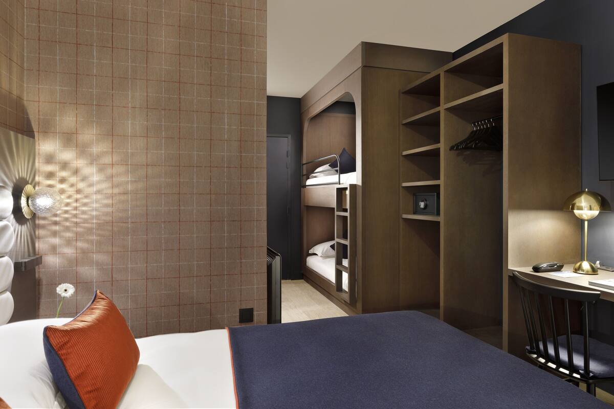 Una habitación de hotel con cama, escritorio, silla, armario y espejo.