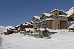 Estância de esqui coberta por neve, com vários edifícios de madeira, incluindo um hotel notável com uma placa.