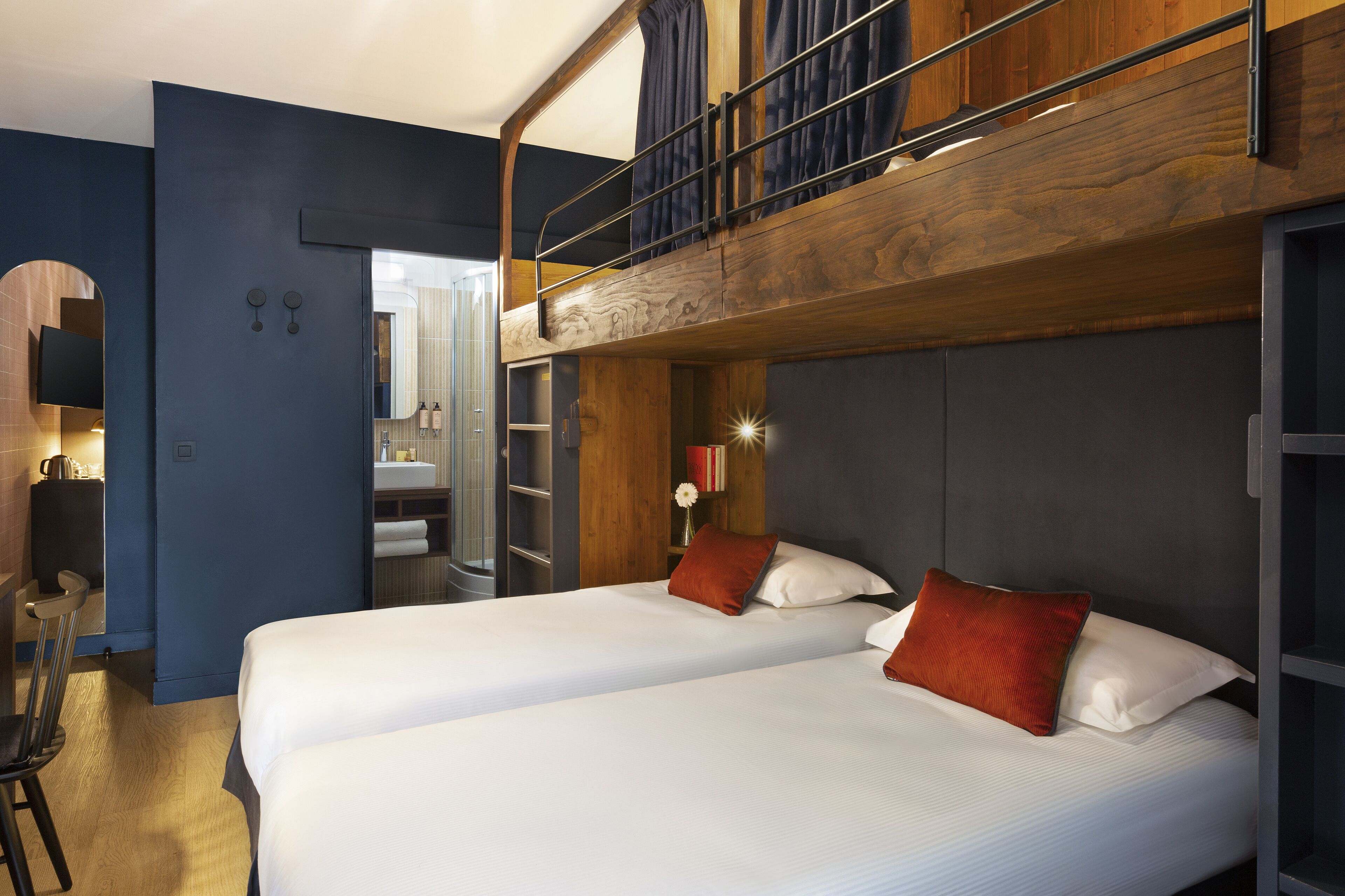 A modern hotel room with a bunk bed, a desk, and a mirror.