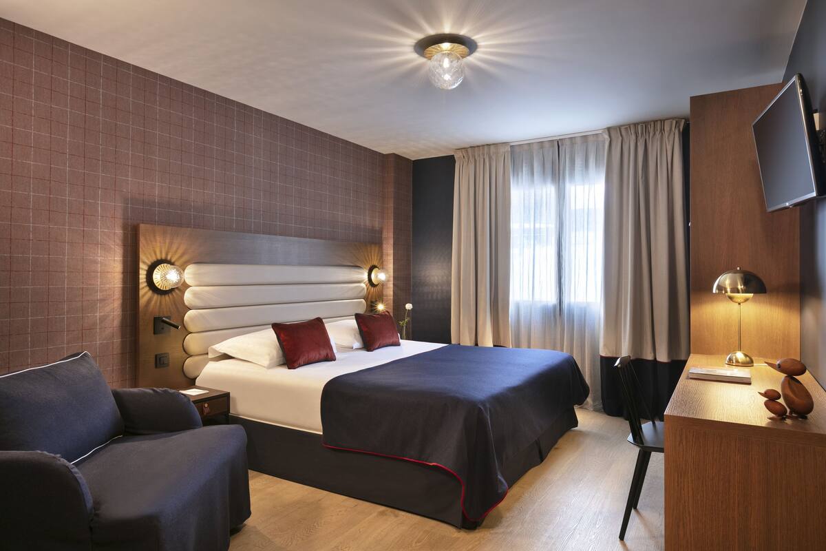 Una habitación de hotel con una cama grande, un escritorio, una silla, un televisor y una lámpara.