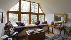 A cozy room with a large bay window, a wooden chest, a bench with cushions, and a small table with books and a lamp. - Brae House Bed & Breakfast (Aberfeldy)